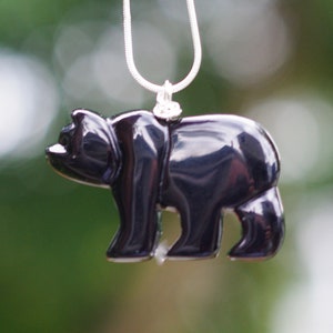 May include: A black onyx bear pendant necklace with a silver chain. The bear is carved in a realistic style and has a shiny, polished finish.
