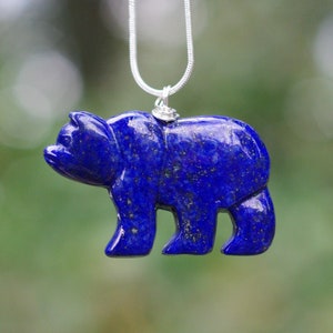 May include: A blue lapis lazuli bear pendant on a silver chain. The bear is carved from a single piece of stone and has a detailed, realistic design.