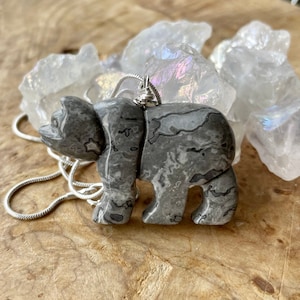 May include: A silver chain necklace with a gray stone bear pendant. The bear is carved from a marbled stone with a gray and white pattern.
