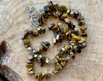 May include: A long necklace made of brown and gold tiger's eye stone chips. The necklace has a silver clasp.