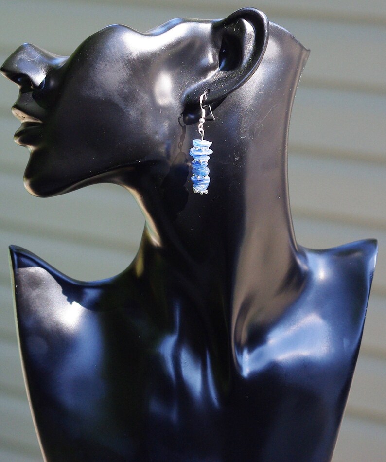 May include: A pair of silver earrings with blue gemstone beads. The earrings are dangling and have a silver hook closure.