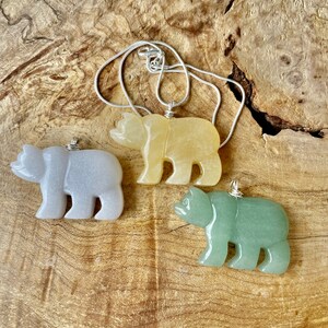 May include: Three carved bear pendants on a silver chain. The bears are made of light gray, yellow, and green stone.