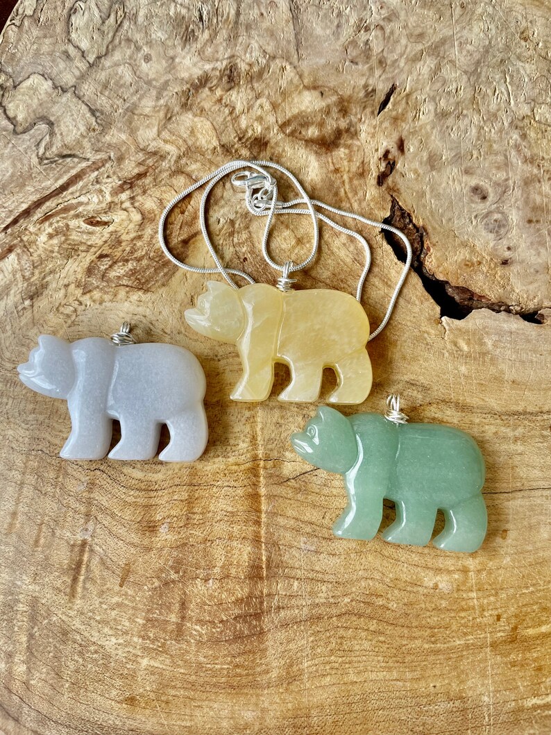 May include: Three carved bear pendants on a silver chain. The bears are made of light gray, yellow, and green stone.
