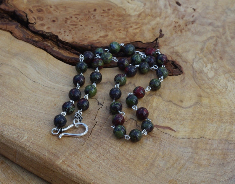 May include: A green and red gemstone beaded necklace with a silver clasp. The necklace is made of round beads and is approximately 20 inches long.