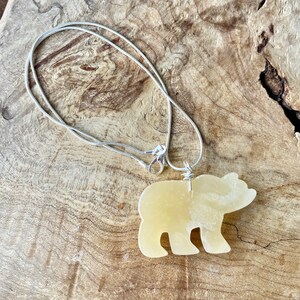 May include: A silver chain necklace with a yellow bear-shaped pendant. The pendant is made of a smooth, polished stone.