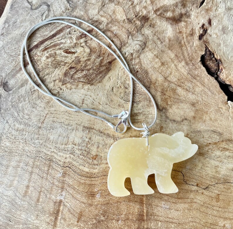 May include: A silver chain necklace with a yellow bear-shaped pendant. The pendant is made of a smooth, polished stone.