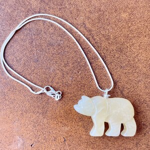May include: A silver chain necklace with a carved yellow bear pendant.