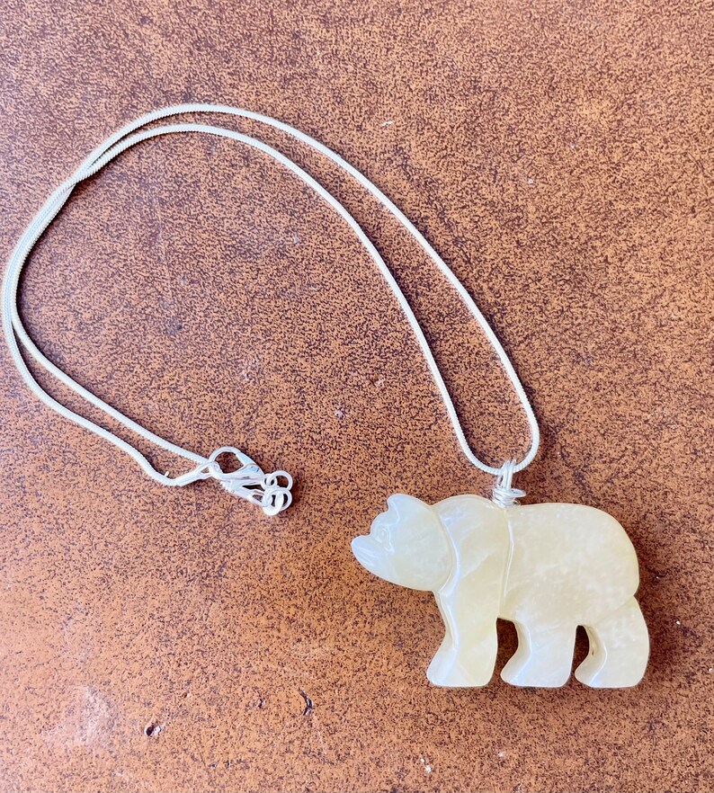 May include: A silver chain necklace with a carved yellow bear pendant.