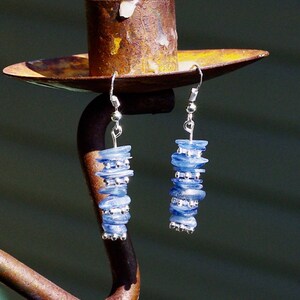 May include: A pair of silver dangle earrings with blue gemstone beads. The earrings are hanging from a rusty metal candle holder.