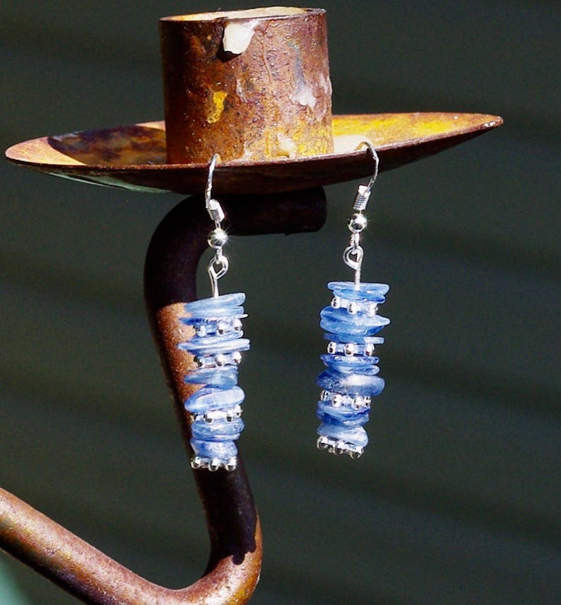 May include: A pair of silver dangle earrings with blue gemstone beads. The earrings are hanging from a rusty metal candle holder.