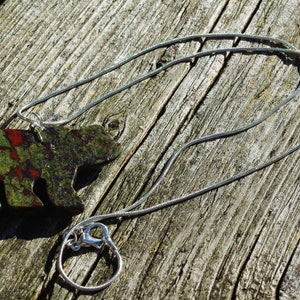 May include: A silver chain necklace with a green, red, and black bear pendant. The bear is made of a mottled stone.