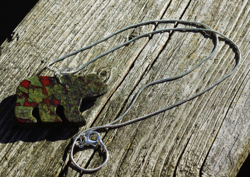 May include: A silver chain necklace with a green, red, and black bear pendant. The bear is made of a mottled stone.