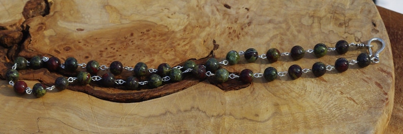 May include: A green, red, and black gemstone necklace with silver chain and clasp.