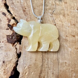 May include: A yellow carved bear pendant on a silver chain. The bear is made of a translucent stone with a slightly cloudy appearance.