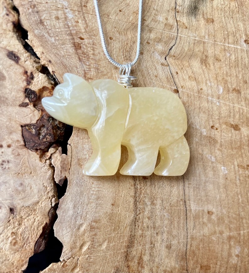 May include: A yellow carved bear pendant on a silver chain. The bear is made of a translucent stone with a slightly cloudy appearance.