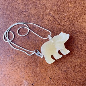 May include: A silver chain necklace with a light yellow bear pendant. The bear is carved from stone and has a smooth, polished finish.