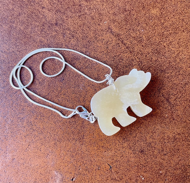 May include: A silver chain necklace with a light yellow bear pendant. The bear is carved from stone and has a smooth, polished finish.