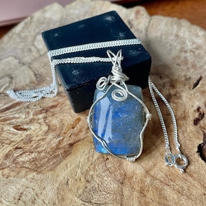 May include: A silver chain necklace with a silver wire wrapped labradorite pendant. The pendant is a rectangular shape with a blue and green iridescent stone.