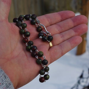May include: A green and brown beaded necklace with a silver clasp. The necklace is made of small, round beads and is strung on a silver chain.