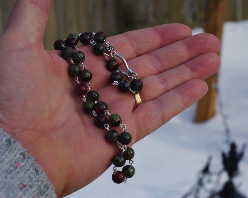 May include: A green and brown beaded necklace with a silver clasp. The necklace is made of small, round beads and is strung on a silver chain.
