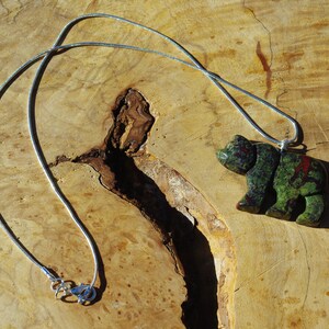 May include: A silver chain necklace with a green and red bear pendant carved from stone.