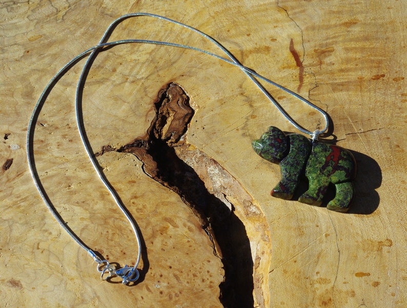 May include: A silver chain necklace with a green and red bear pendant carved from stone.