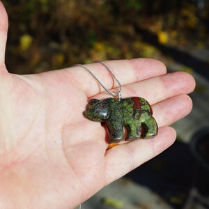May include: A green, red, and black bear pendant carved from a stone with a silver chain.