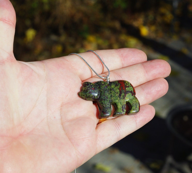 May include: A green, red, and black bear pendant carved from a stone with a silver chain.