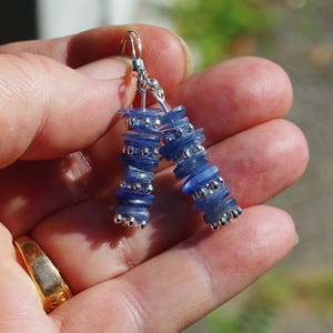 May include: A pair of silver earrings with blue gemstone beads. The beads are stacked and have a slightly iridescent finish.