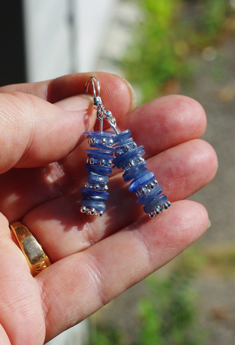 May include: A pair of silver earrings with blue gemstone beads. The beads are stacked and have a slightly iridescent finish.