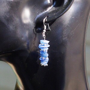 May include: A pair of silver dangle earrings with blue glass beads. The beads are stacked on top of each other and have a slightly iridescent finish.