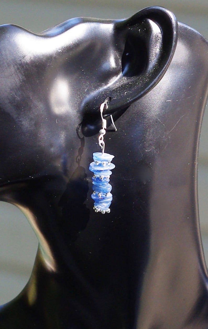 May include: A pair of silver dangle earrings with blue glass beads. The beads are stacked on top of each other and have a slightly iridescent finish.