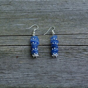 May include: A pair of silver earrings with blue gemstone beads. The beads are stacked and have a faceted, irregular shape.