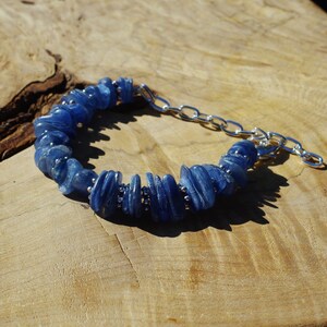 Op de afbeelding: Een blauwe kyanite-stenen armband met een zilveren kettingsluiting. De armband is gemaakt van gladde, platte en licht gebogen kyanite-stenen.