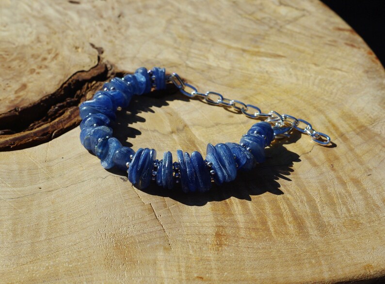 Op de afbeelding: Een blauwe kyanite-stenen armband met een zilveren kettingsluiting. De armband is gemaakt van gladde, platte en licht gebogen kyanite-stenen.