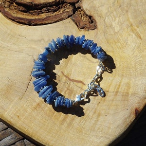 Op de afbeelding: Een blauwe edelsteen armband met een zilveren sluiting. De armband is gemaakt van kleine, platte, blauwe stenen die op elkaar gestapeld zijn.