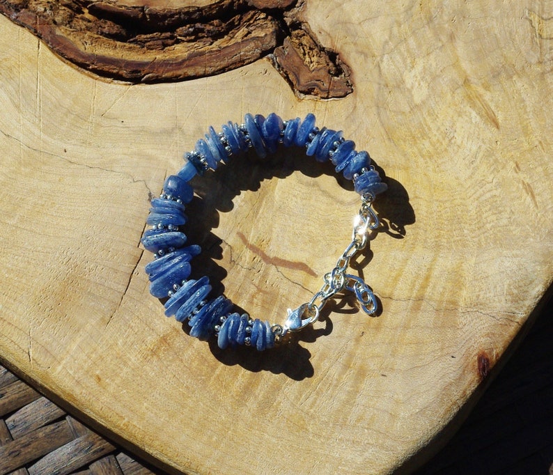 Op de afbeelding: Een blauwe edelsteen armband met een zilveren sluiting. De armband is gemaakt van kleine, platte, blauwe stenen die op elkaar gestapeld zijn.