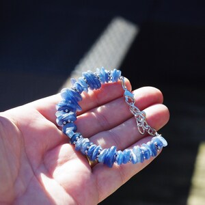 Op de afbeelding: Een blauwe kyanite-stenen armband met een zilveren sluiting. De armband is gemaakt van kleine, onregelmatige stukjes kyanite die aan elkaar geregen zijn op een zilveren ketting.