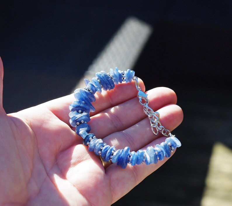 Op de afbeelding: Een blauwe kyanite-stenen armband met een zilveren sluiting. De armband is gemaakt van kleine, onregelmatige stukjes kyanite die aan elkaar geregen zijn op een zilveren ketting.