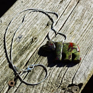 May include: A silver chain necklace with a green, red, and black stone bear pendant.