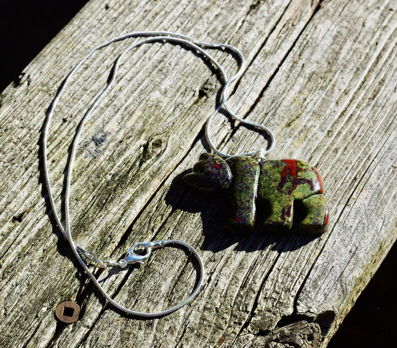 May include: A silver chain necklace with a green, red, and black stone bear pendant.
