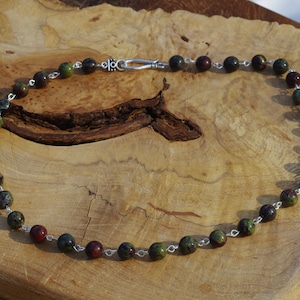 May include: A necklace made of green, red, and black gemstone beads with silver chain links and a silver clasp.