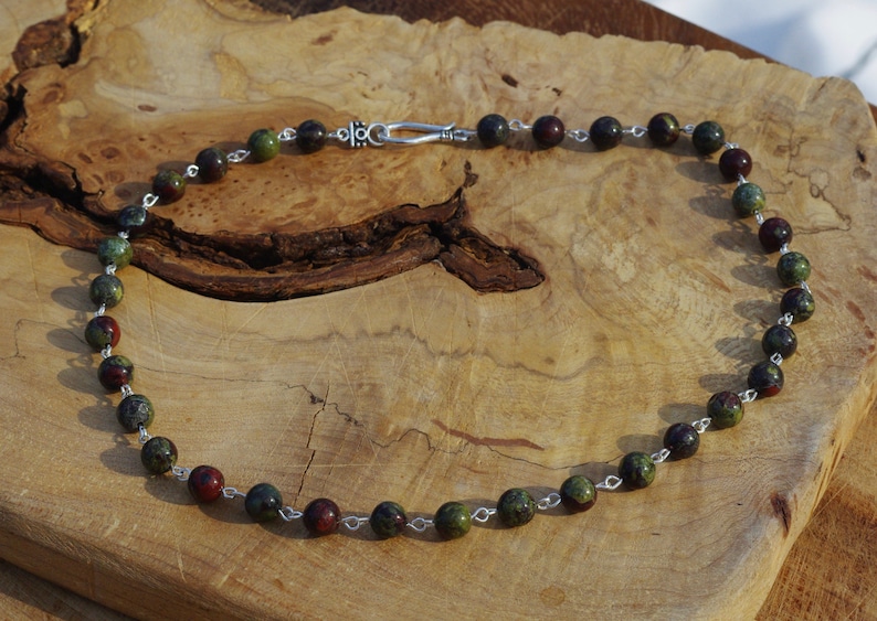 May include: A necklace made of green, red, and black gemstone beads with silver chain links and a silver clasp.