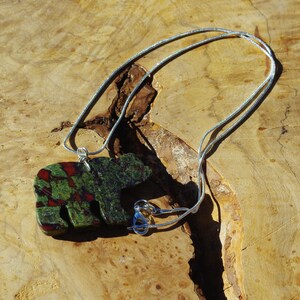 May include: A silver chain necklace with a green, red, and black stone bear pendant.