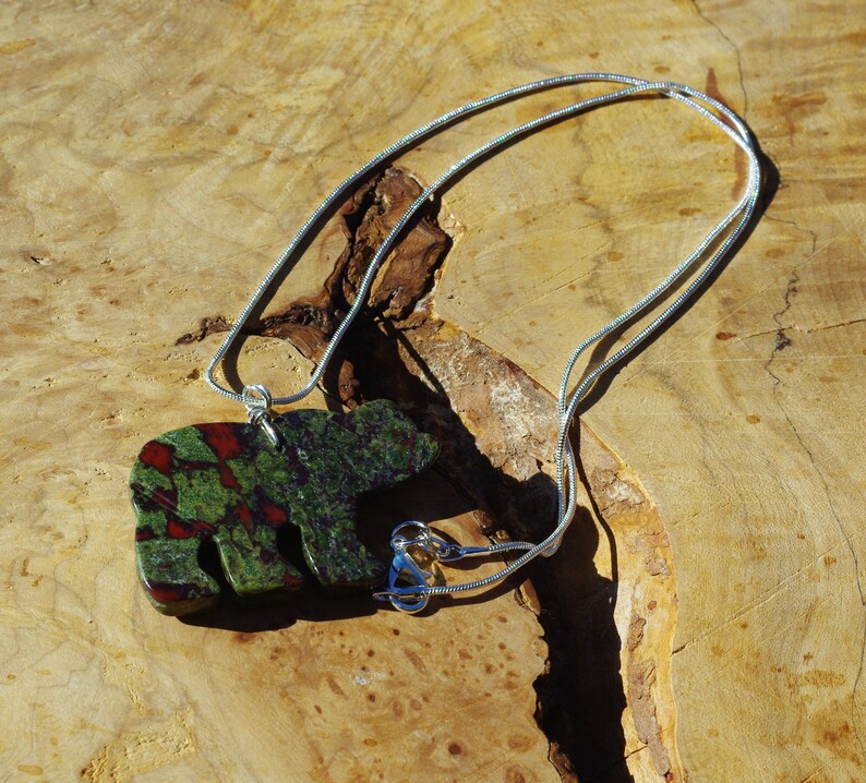 May include: A silver chain necklace with a green, red, and black stone bear pendant.