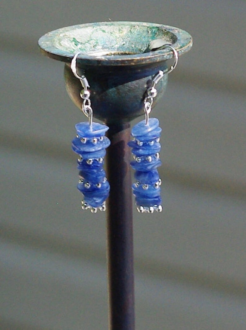 May include: A pair of dangle earrings with blue and silver beads. The earrings are hanging from a metal stand.