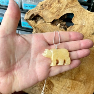 May include: A yellow carved bear pendant on a silver chain. The pendant is made of a translucent stone and is about 2 inches tall.
