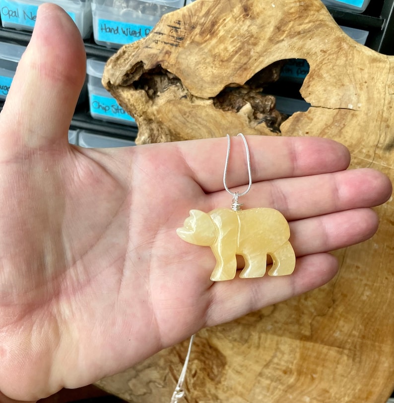 May include: A yellow carved bear pendant on a silver chain. The pendant is made of a translucent stone and is about 2 inches tall.