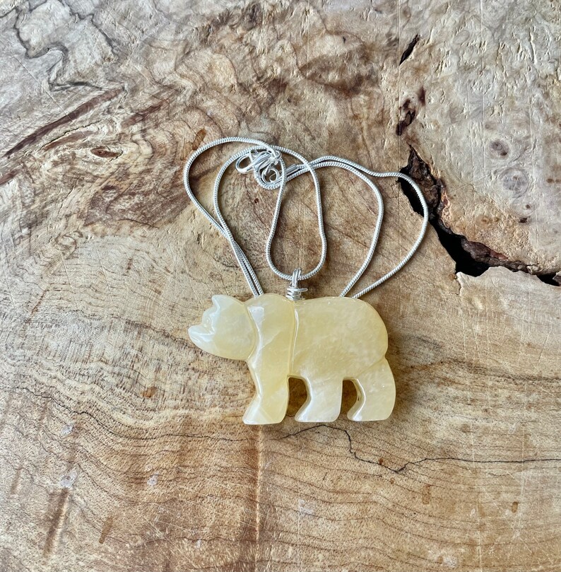 May include: A yellow carved bear pendant on a silver chain necklace. The pendant is made of a smooth, polished stone.
