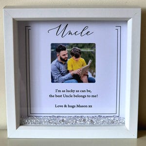 以下が含まれることがあります： 白いフレームに入った写真で、筆記体で「Uncle」と書かれています。 写真には、本を読む男性と子供の写真が含まれています。 写真の下のテキストは「I'm as lucky as can be, the best Uncle belongs to me!」と「Love & hugs Mason xx.」と書かれています。
